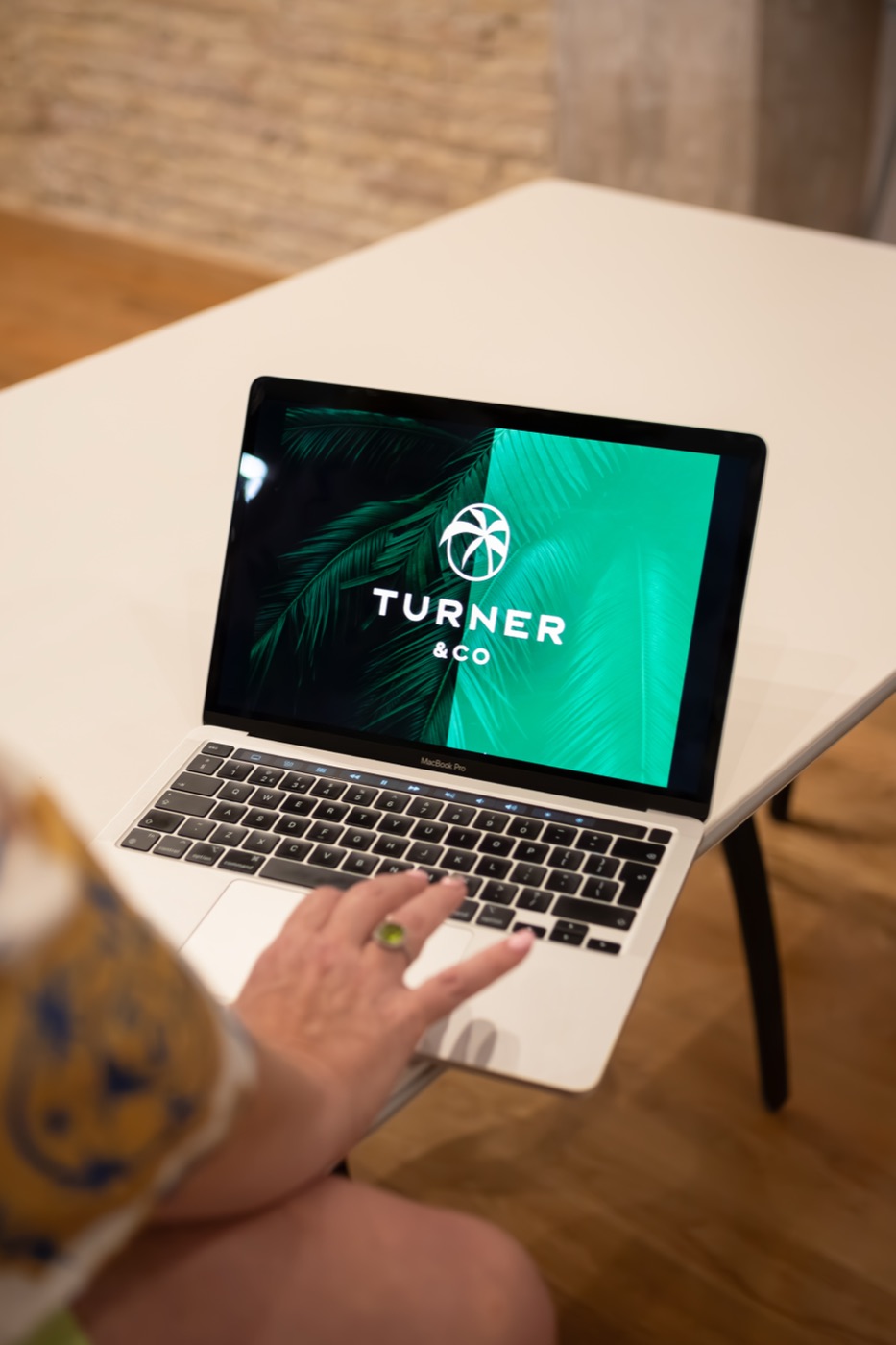 A laptop on a white table showing the Turner & Co palm logo